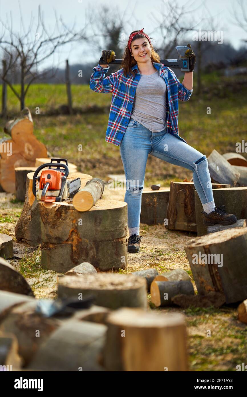 Starke Holzfällerin mit ihrer Axt und ihrer Kettensäge Riesige abgesägte Holzstämme Stockfoto