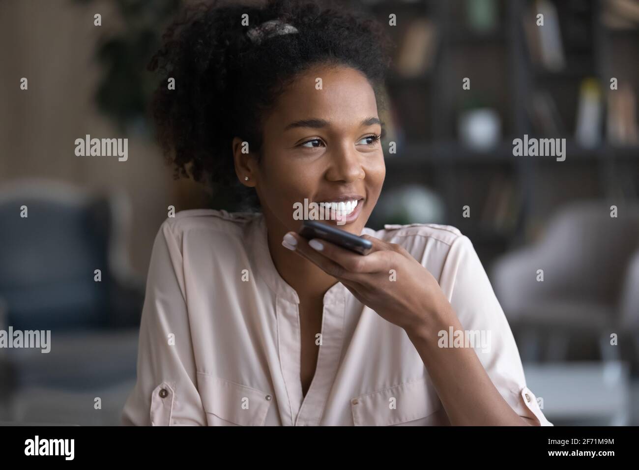 Lächelnde Birazialfrau zeichnet Audionachrichten auf dem Handy auf Stockfoto