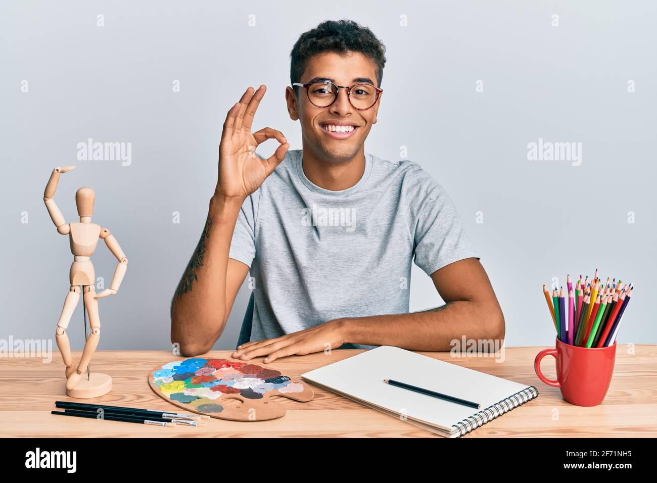 Junge gutaussehende afroamerikanische Mann Maler sitzende Palette und Kunst menschlich lächelnd positive tun ok Zeichen mit Hand und Fingern. Erfolgreiche expressio Stockfoto