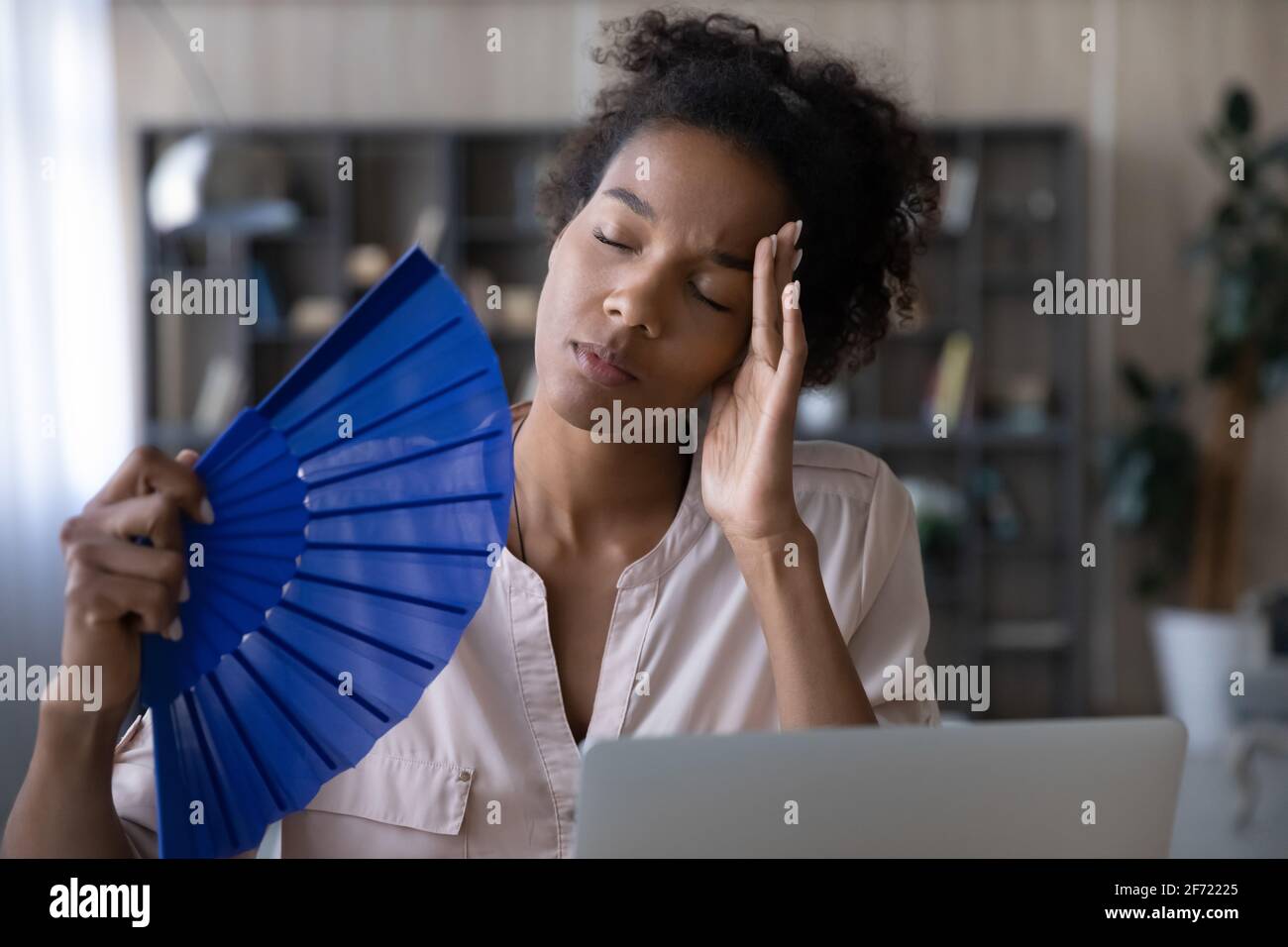 Unwohl Birazialfrau winken mit Handventilator, der am Computer arbeitet Stockfoto