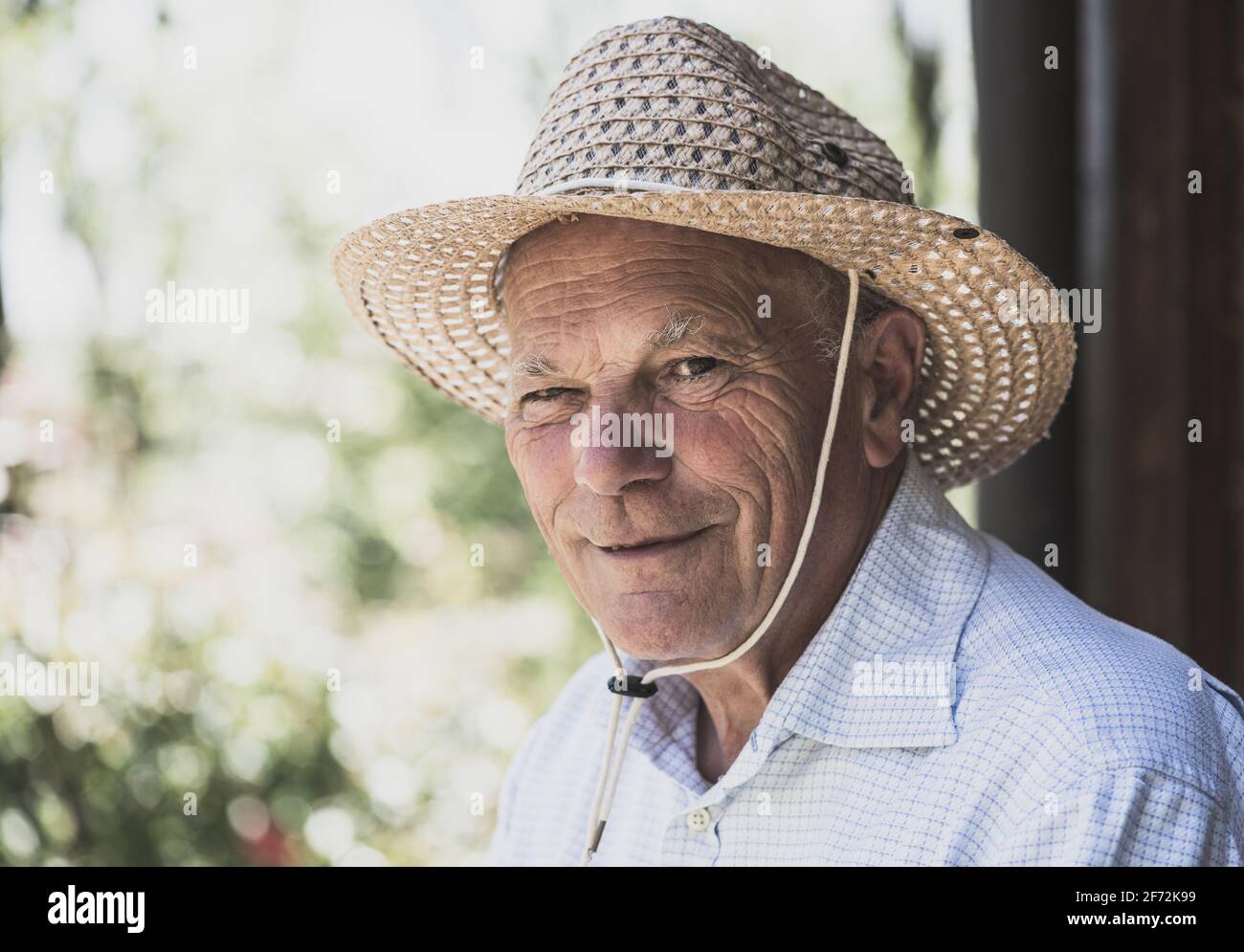Porträt eines älteren lächelnden Mannes mit Strohhut, der auf die Kamera schaute. Ältere Menschen Lebensstil, Abend Glühfilter. Stockfoto