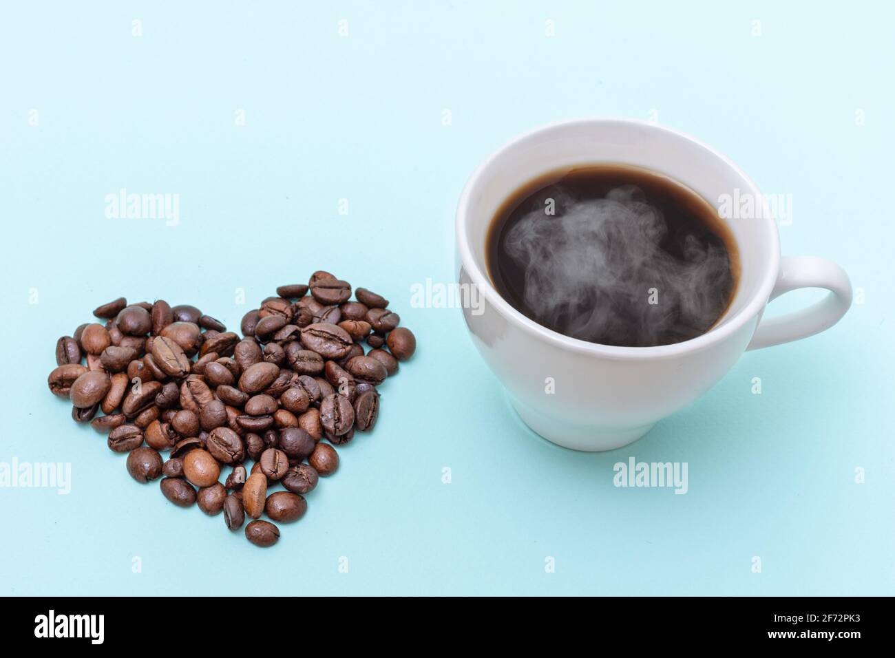 Dampfende Kaffeetasse, herzförmige Kaffeebohnen auf blauem Hintergrund, Platz zum Kopieren. Morgenkaffee für die Liebsten. Stockfoto