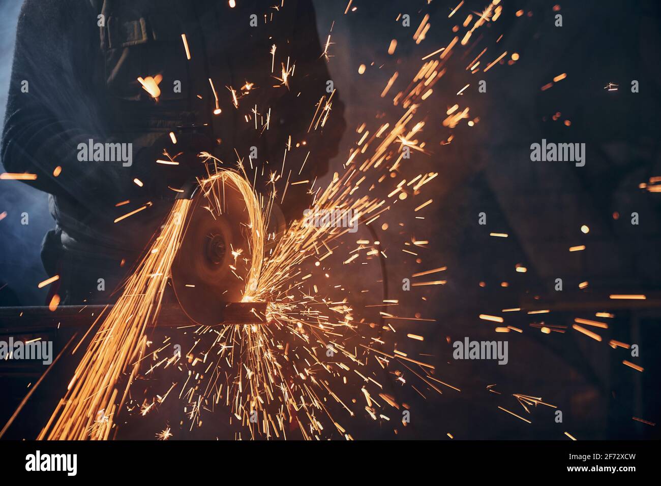 Nahaufnahme eines Mitarbeiters, der Metallrohre mit großen gelben Funken schneidet. Konzept der Arbeit mit Winkelschleifer und Polieren oder Schweißen Metall im Werk. Stockfoto