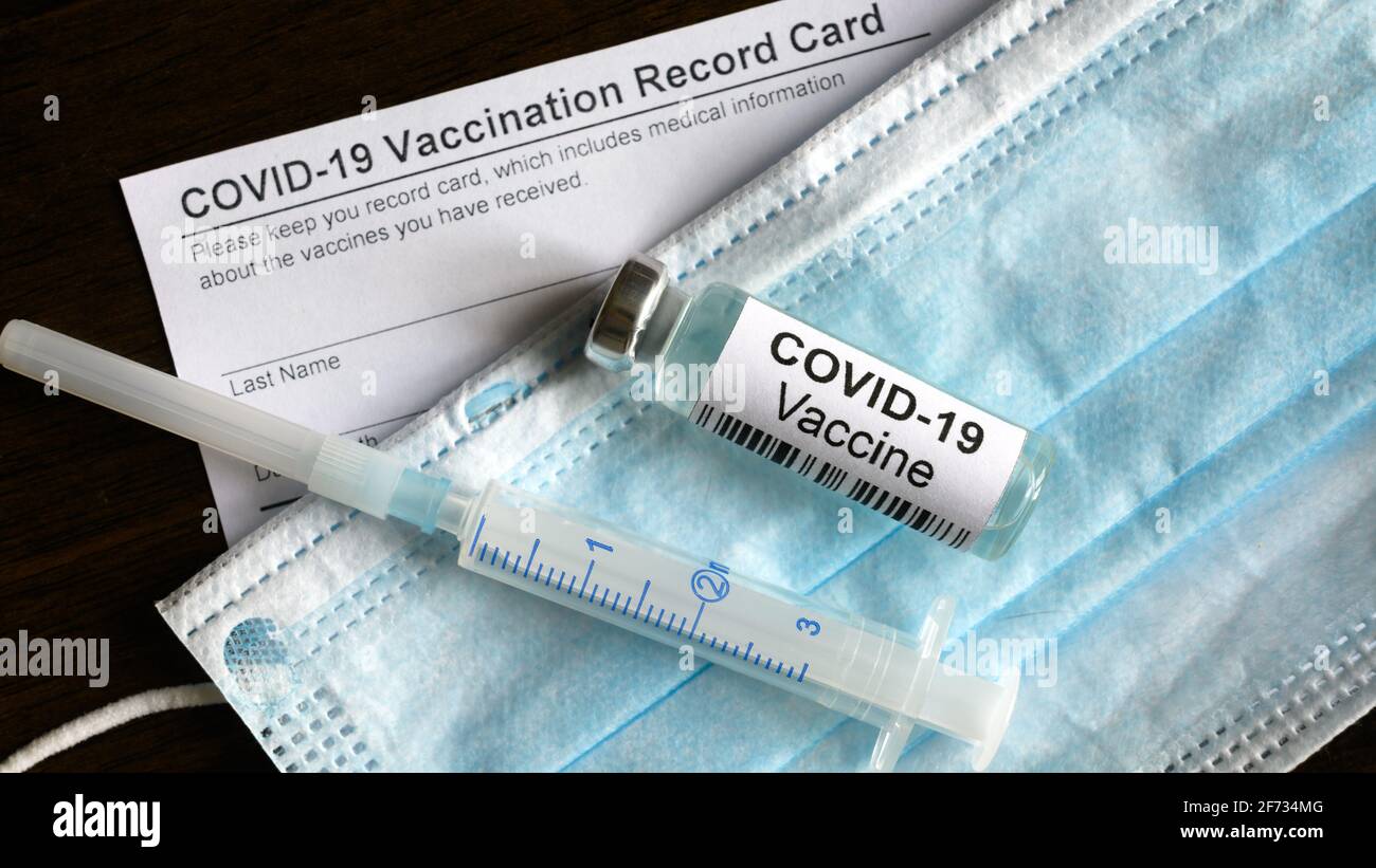 COVID-19-Impfstoffflasche, Spritze, OP-Maske und Coronavirus-Impfkarte auf dem Schreibtisch, Draufsicht auf Corona-Virus-Impfstoff und Impfschutz Stockfoto