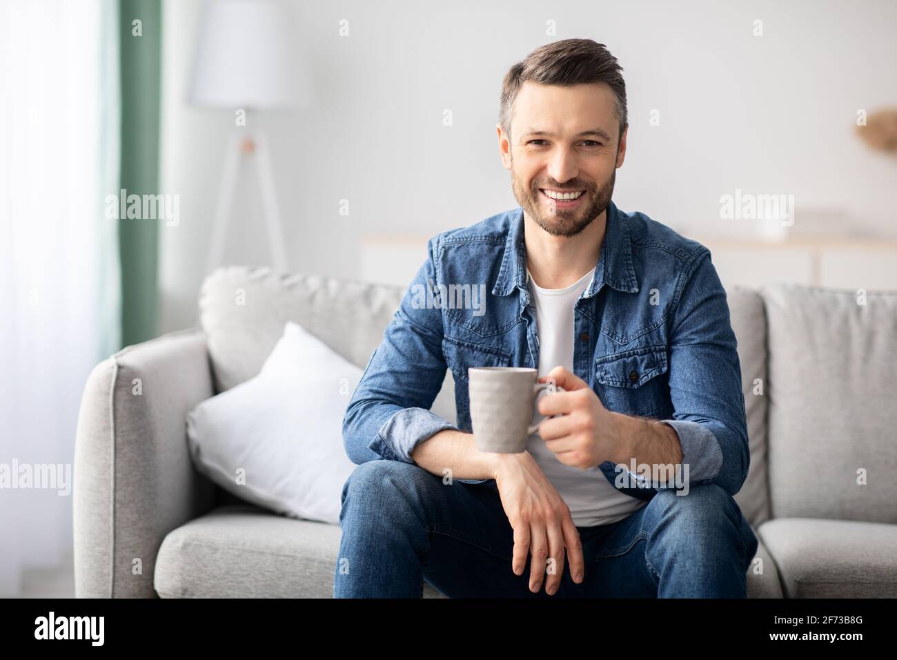 Ein schöner Mann, der im Wohnzimmer Kaffee trinkt Stockfoto