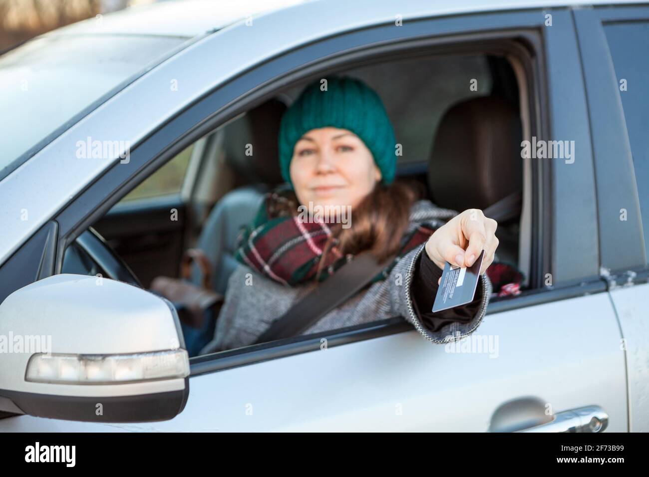 Eine Autofahrerin, die bargeldlose Zahlungen per Kreditkarte in ihrem Auto macht und dabei die Kamera anschaut Stockfoto