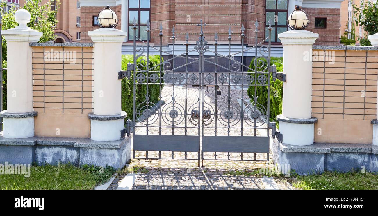 Schmiedeeiserne Tore für einen Tempel oder eine Kirche. Bild von einem schönen dekorativen gusseisernen schmiedeeisernen Zaun und Tore mit kunstvollen Schmieden und Steinsäulen Stockfoto