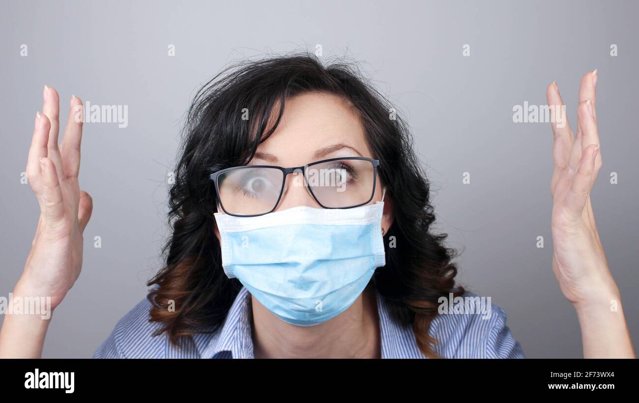 Frau trägt Schutzmaske gegen Coronavirus und vernebelte Brille. Frau in einer Maske, die schockiert mit den Händen nach oben oder besorgt aussieht. Medizinische Maske, Klo Stockfoto