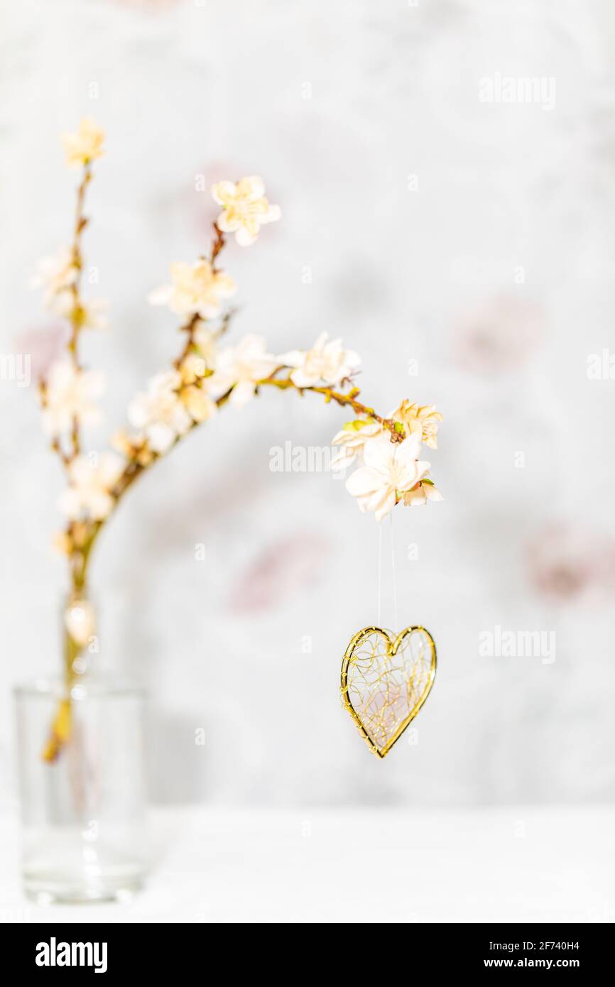 Ein goldenes Herz hängt an einem Frühlingszweig, der ist Mit Blüten bedeckt Stockfoto