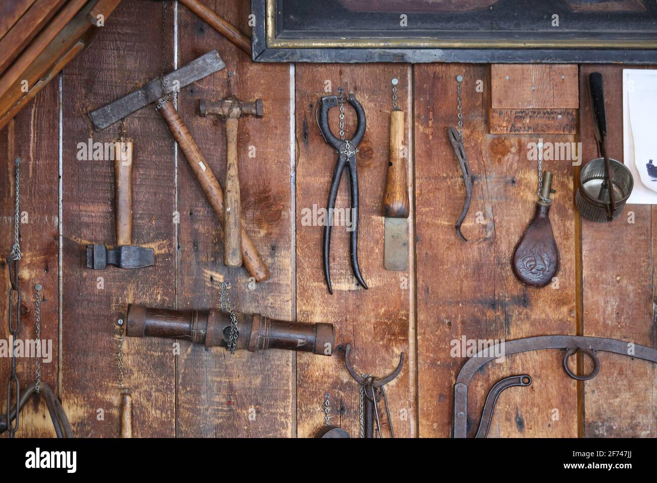 Rustikales Land alte antike Metall-Farm Werkzeuge einschließlich Hammer, Eisenklemme, Tasse, und rostigen handwerklichen Gegenstände hängen an einer alten Holz Scheune Schuppen Wand Stockfoto