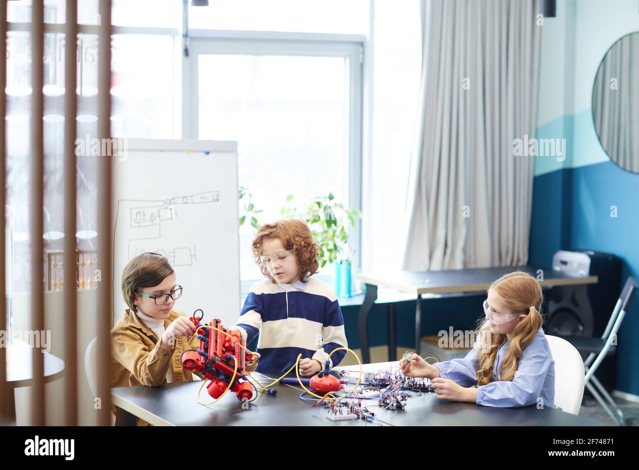 Portrait von drei niedlichen Kindern, die zusammen Roboter bauen, während sie den Ingenieurunterricht in der Entwicklungsschule genießen und Platz kopieren Stockfoto