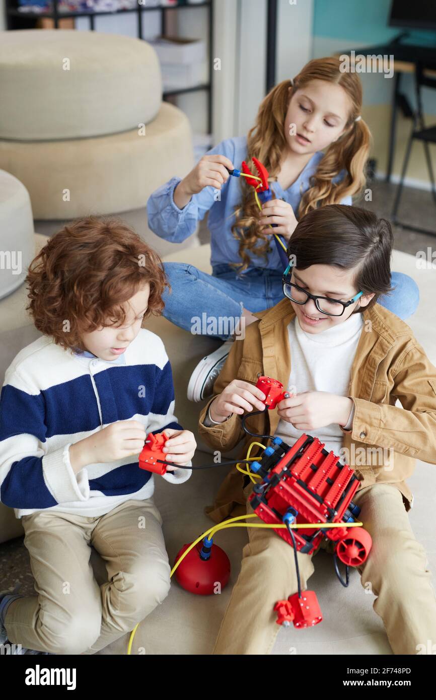 Vertikales Porträt von drei Kindern, die während des Spiels mit der Robotermaschine spielen Engineering-Klasse in der Entwicklungsschule Stockfoto
