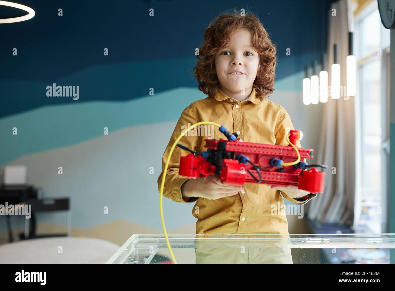 Porträt eines niedlichen, lockigen Jungen, der Robo-Boot ins Wasser setzt, während er im Robotik-Labor in der Schule mit Technologie experimentiert und den Raum kopiert Stockfoto