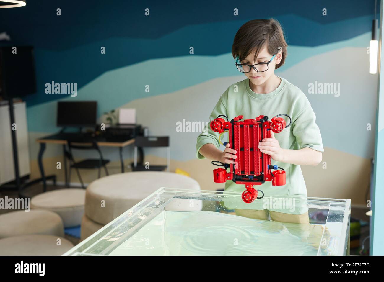 Porträt eines Jungen, der Robo-Boot ins Wasser setzt, während er im Robotik-Labor in der Schule mit Technologie experimentiert, Kopierraum Stockfoto