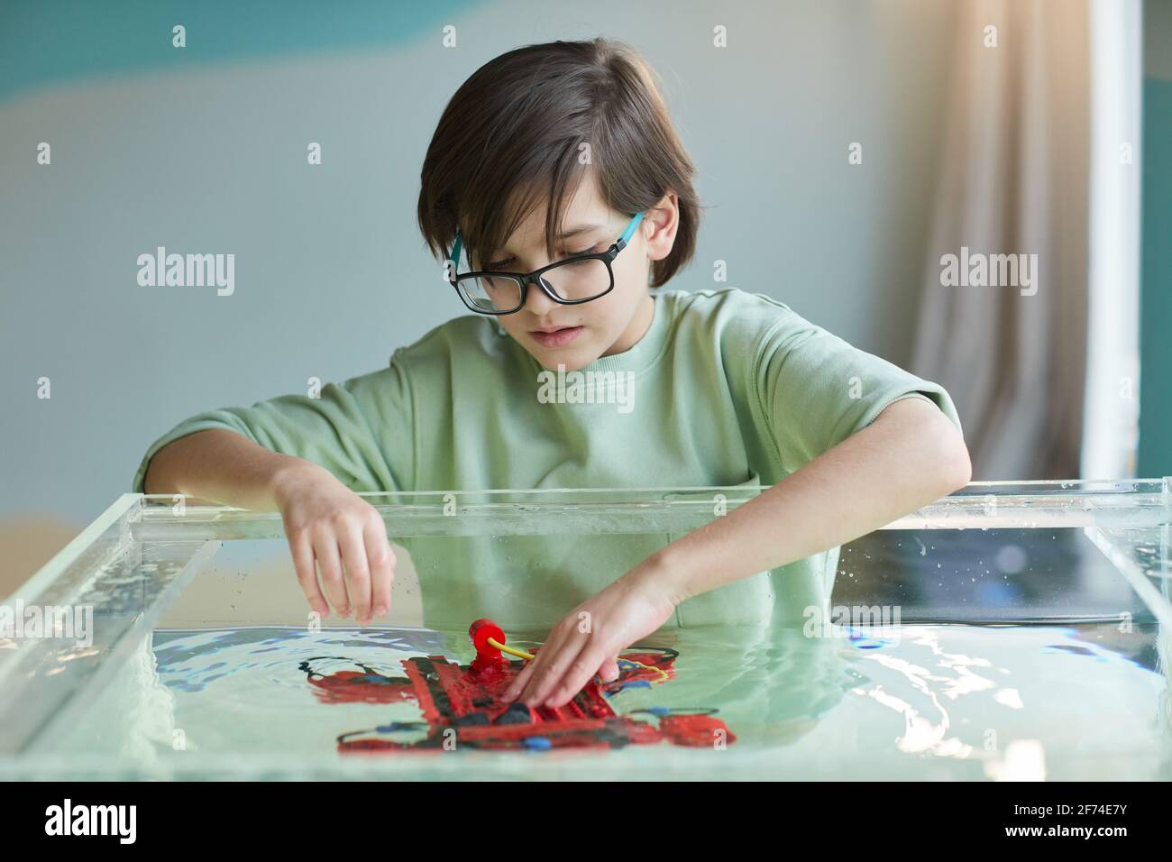 Porträt eines Jungen, der beim Experimentieren ein Robo-Boot ins Wasser setzt Mit Technologie im Robotik-Labor in der Schule Stockfoto