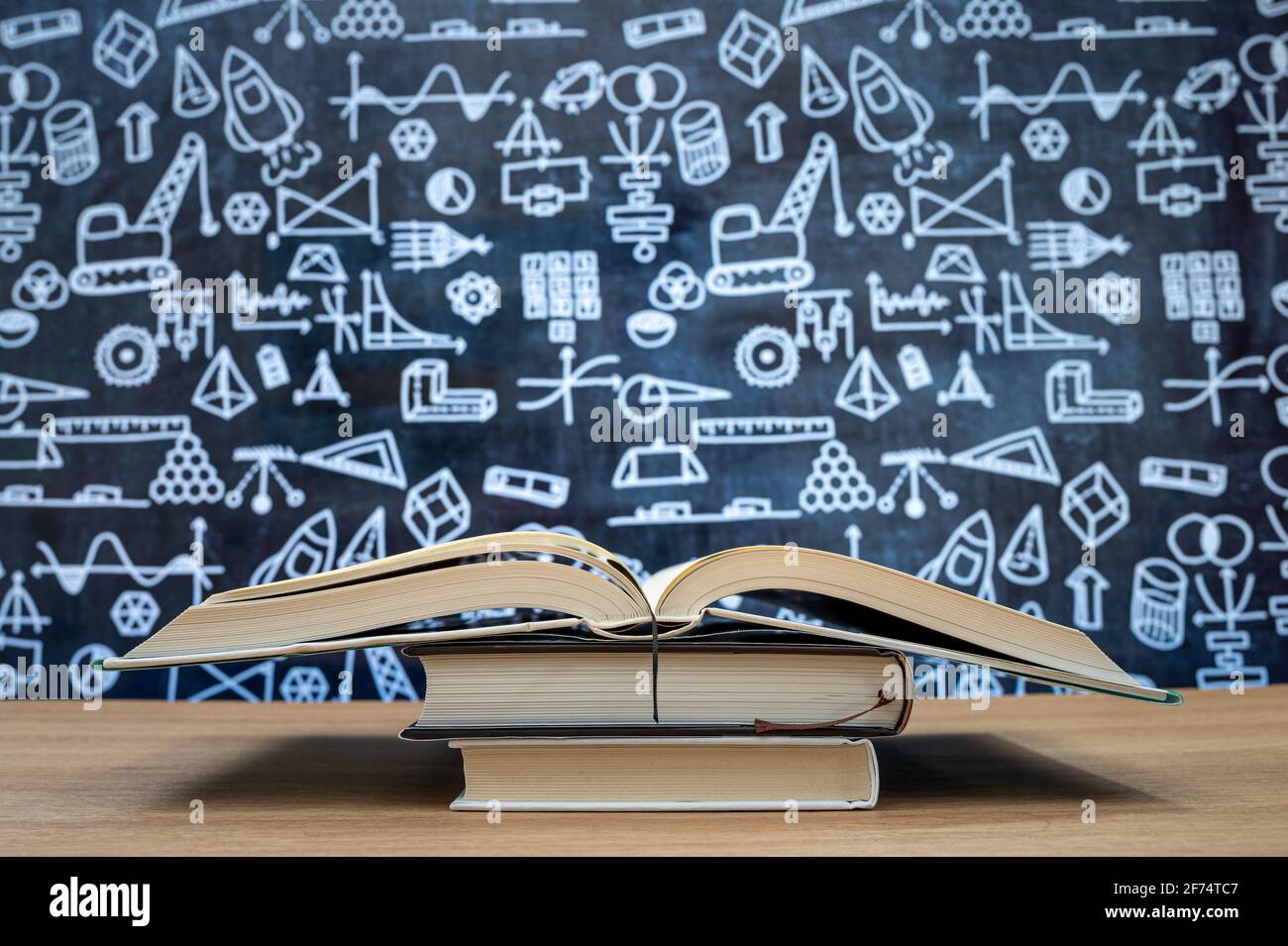 Tafel mit handgezeichneten Symbolen für mathematische Berechnungen. Bücher auf dem Schreibtisch gestapelt. Bildungskonzept. Stockfoto