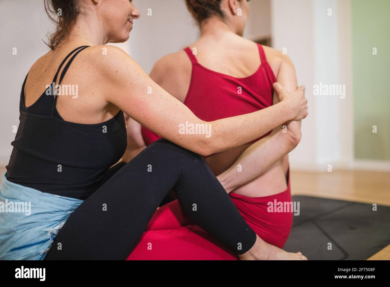 Crop weibliche Ausbilderin unterstützt Frau bei Twist während Yoga-Training auf Sportmatte im Studio Stockfoto