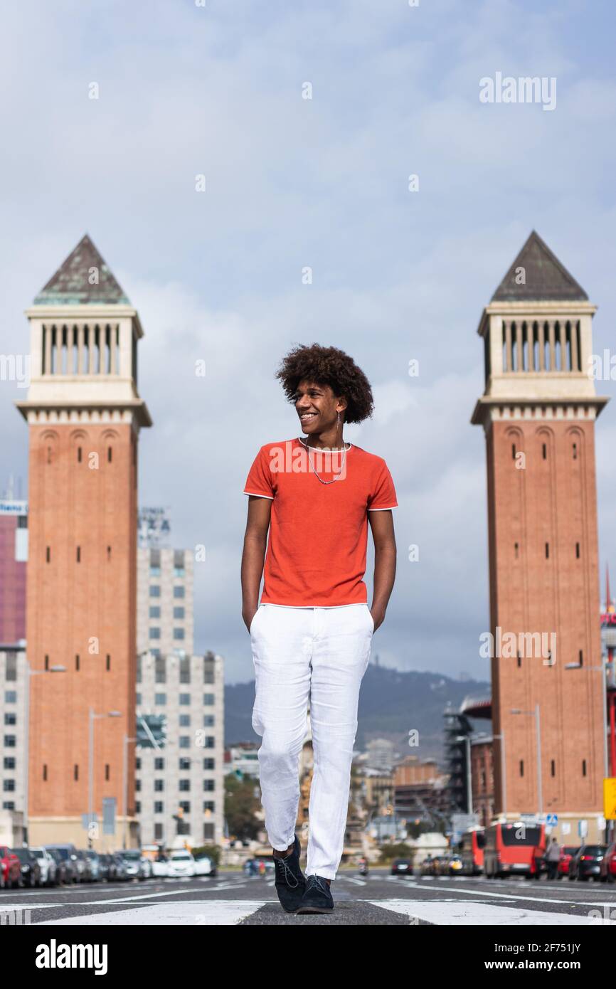 Voller Körper von selbstbewussten jungen schwarzen männlichen tausendjährigen mit Afro-Haare in stilvoller Kleidung, die mit den Händen auf der Straße laufen In Taschen in der Nähe der Venetian Towers i Stockfoto