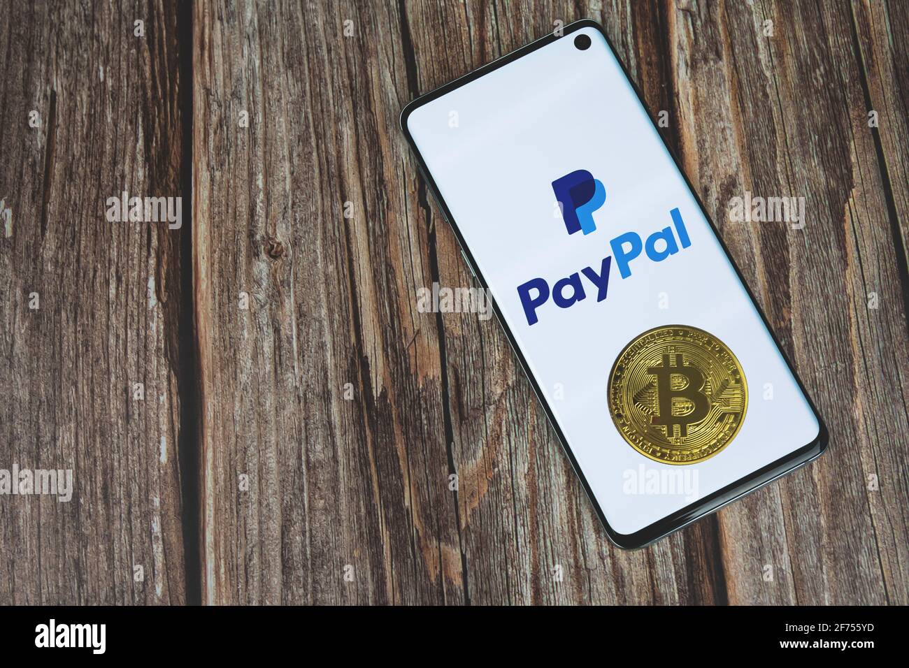 PayPal-Logo auf Telefonbildschirm mit Bitcoin Kryptowährung Münze auf Holzhintergrund mit Kopierraum. Kasse mit Crypto-Konzept Stockfoto