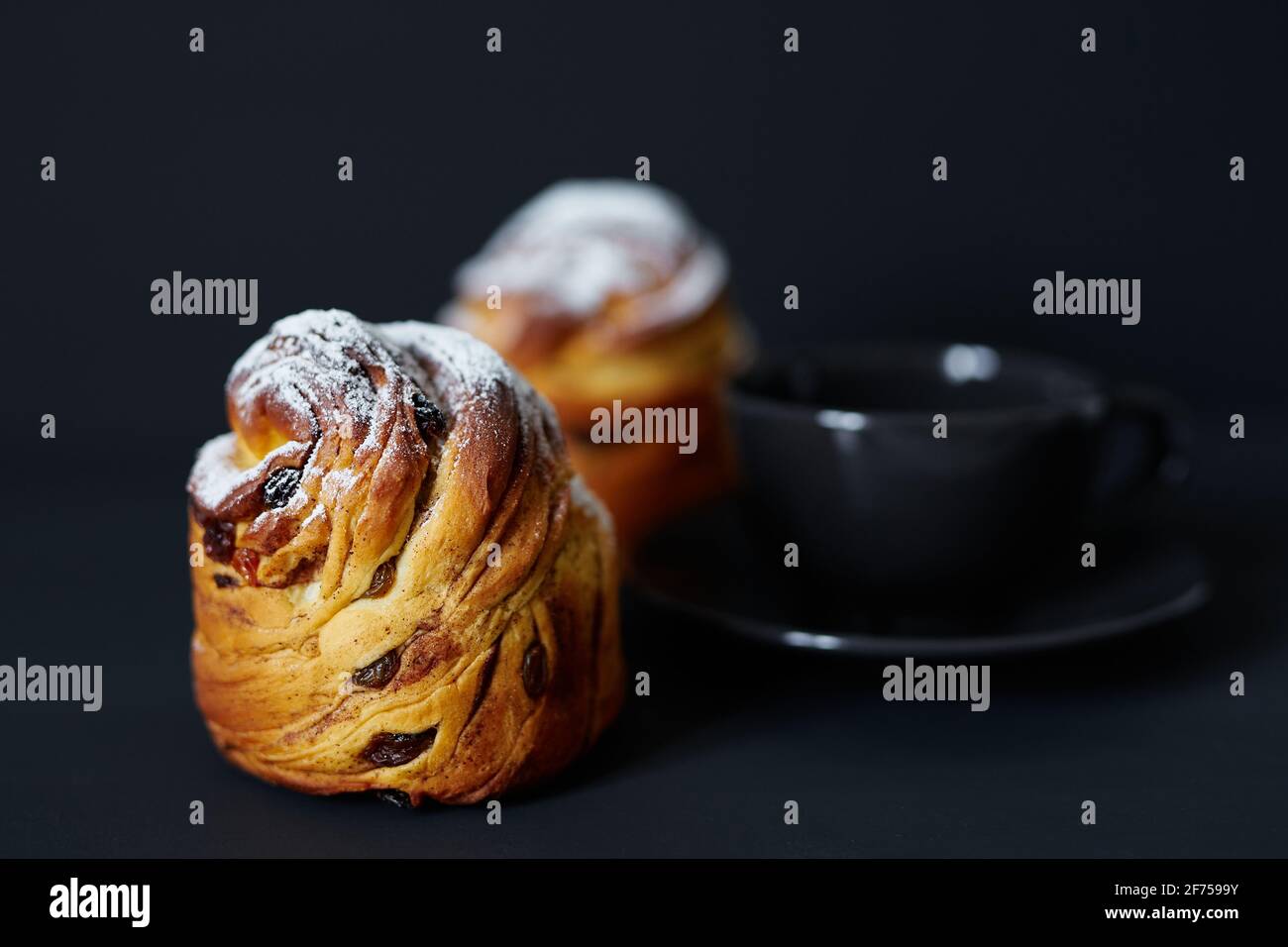 Frisches Oster-Pie- oder Bäckerkonzept. Süße Cruffins mit Rosinen und weißem Zuckerpulver darauf und eine schwarze Tasse Kaffee in der Nähe. Schwarzer Hintergrund. Hochwertige Fotos Stockfoto