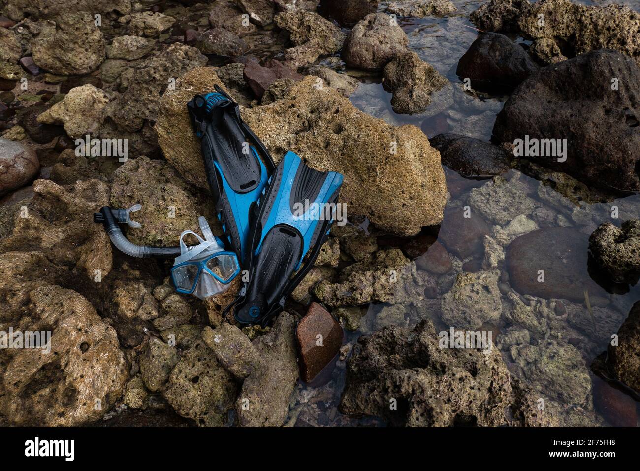 Während eines Urlaubs ruht eine Reihe blauer Masken, Schnorchel und Flossen auf Felsen am Ufer der Insel Stockfoto