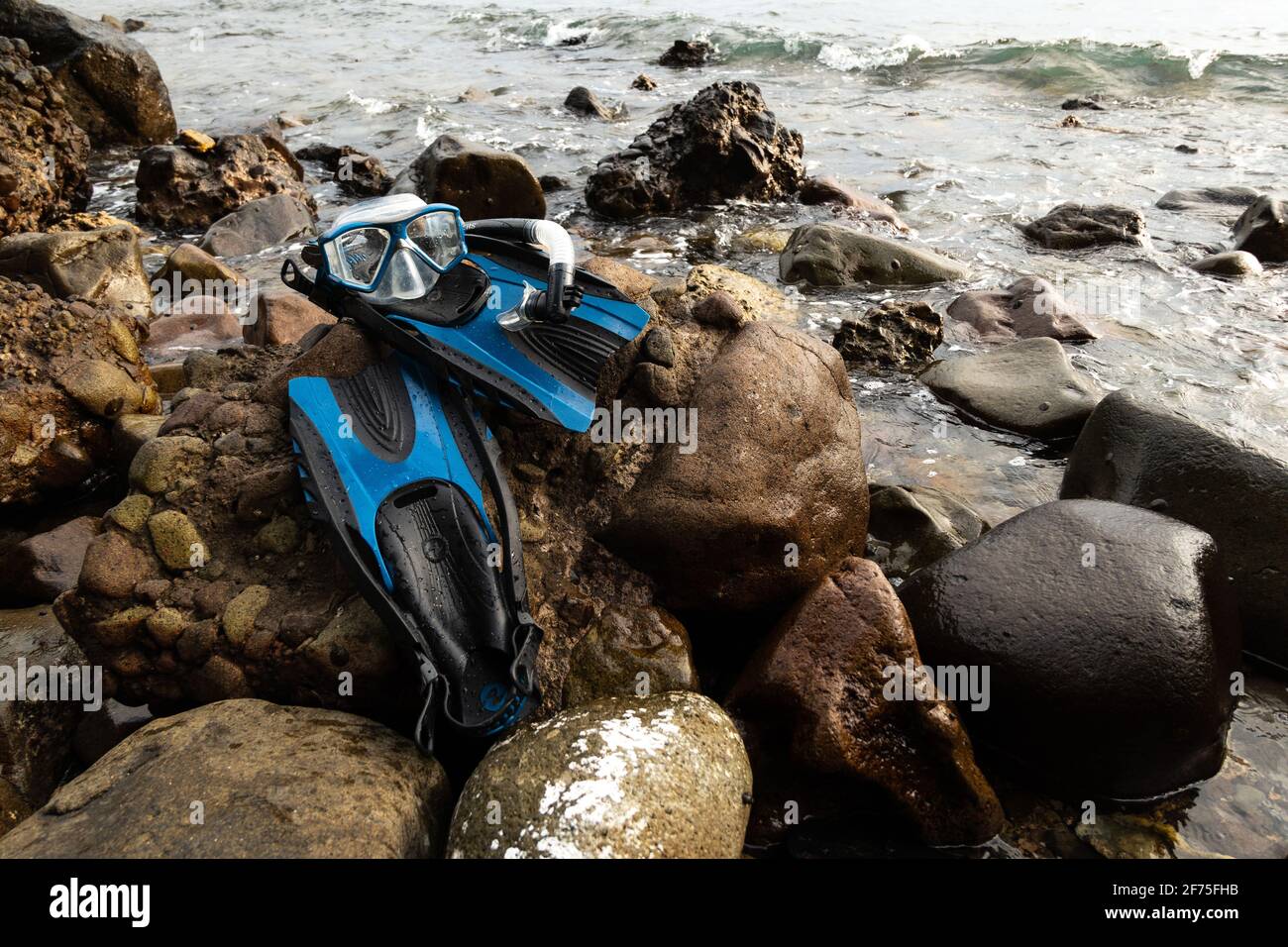 Während eines Urlaubs ruht eine Reihe blauer Masken, Schnorchel und Flossen auf Felsen am Ufer der Insel Stockfoto