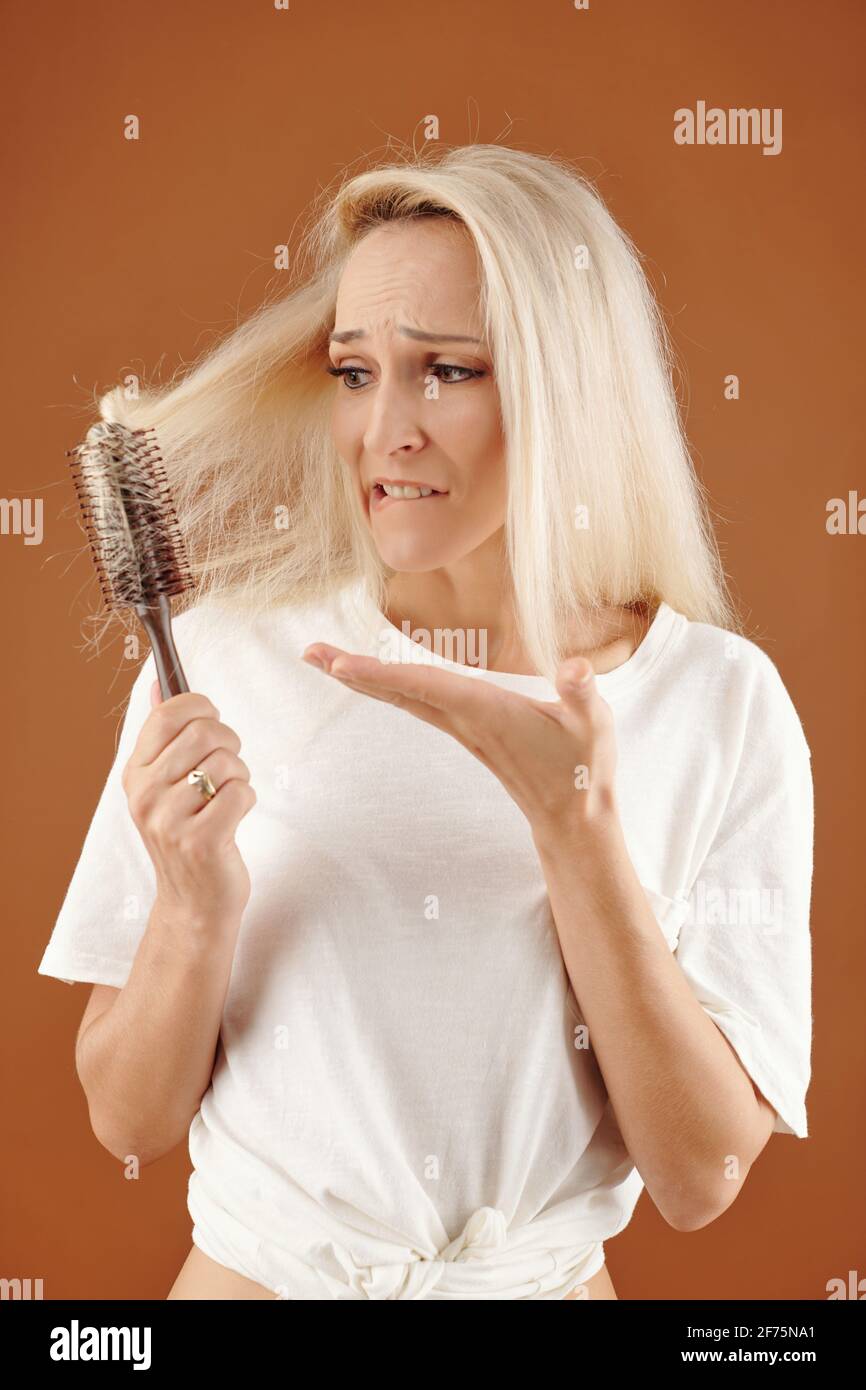 Junge Frau unglücklich mit ihrem trocken gefärbten blonden Haar verwickelt  In der Bürste Stockfotografie - Alamy