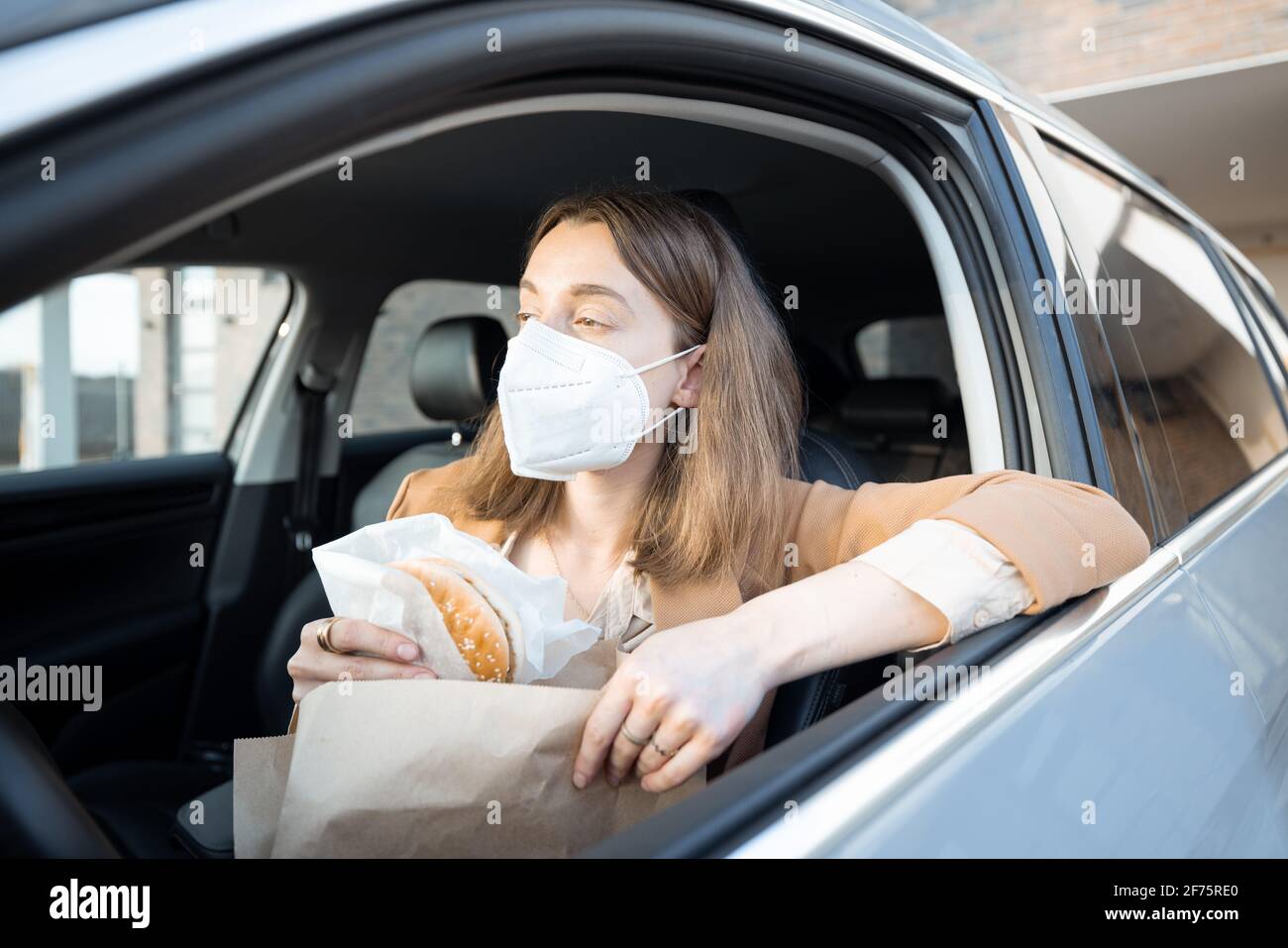 Eine junge Frau mit Schutzmaske auf ihrem Gesicht nahm die Bestellung des Essens auf und holte sich einen Burger aus dem Paket. Gesundheitswesen, Virenschutz. Stockfoto