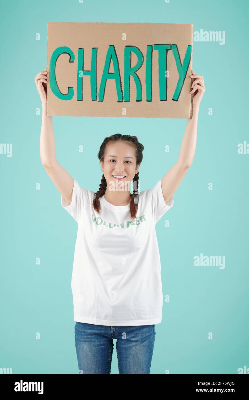 Studio-Porträt einer glücklichen jungen asiatischen Freiwilligen, die eine Wohltätigkeitsorganisation veranstaltet schild über ihrem Kopf und lächelt der Kamera zu Stockfoto