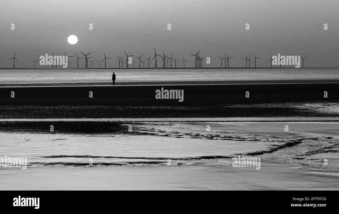 Schwarz-Weiß-Bild eines Eisernen Mannes, der den Sonnenuntergang über dem Windpark Burbo Bank vor dem Crosby Beach beobachtet. Dies ist einer der hundert Eisenmänner-Sta Stockfoto