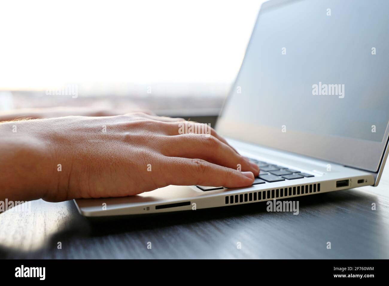 Mann, der an der Laptop-Tastatur in der Nähe des Fensters arbeitet, männliche Hände aus der Nähe. Gemütlicher Arbeitsplatz, Konzept der Online-Kommunikation, Büro- oder Heimarbeit Stockfoto
