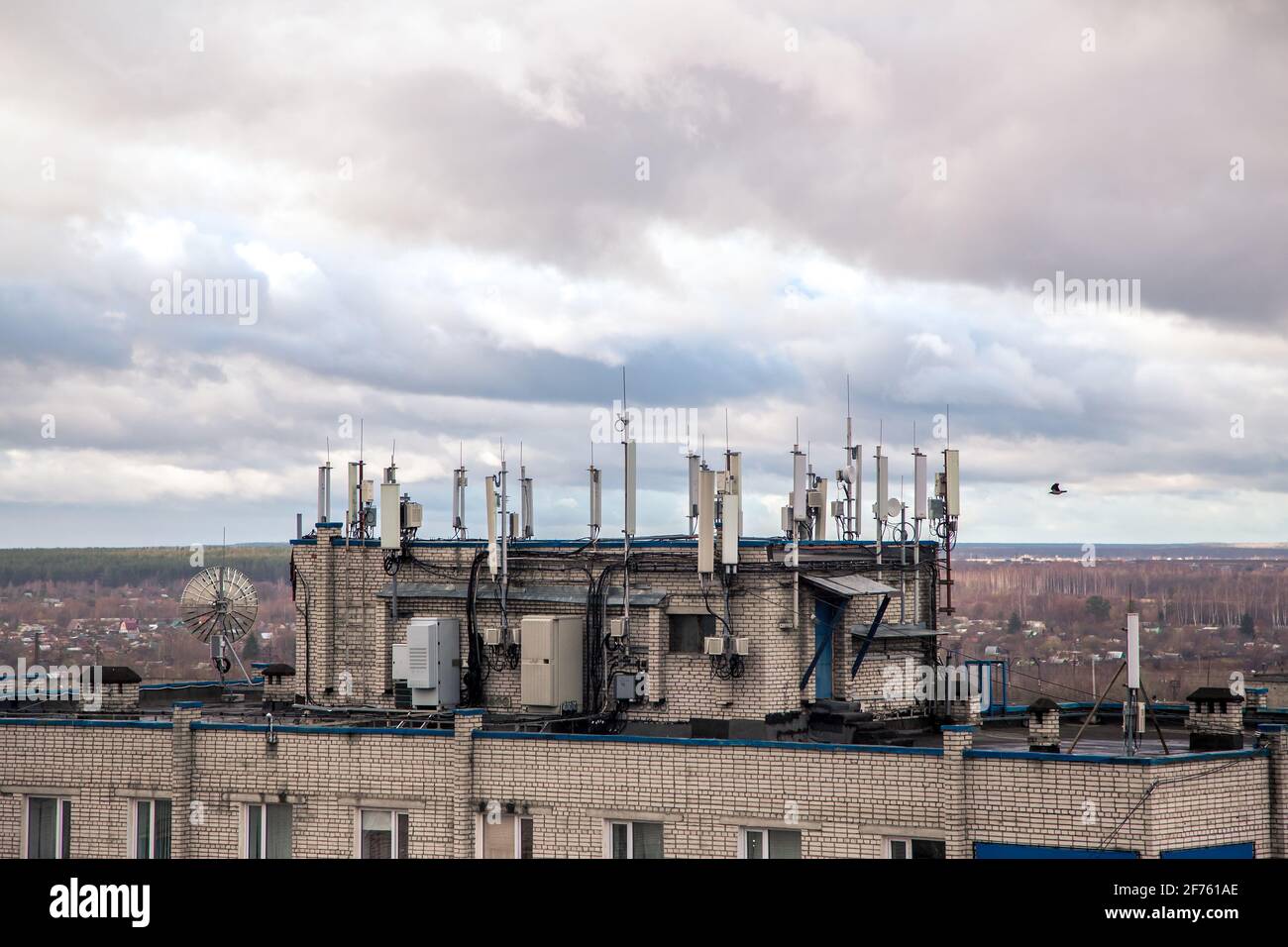 Antennen für Funksender auf dem Dach eines Hochhauses. Die Fassade des Hauses mit Fenstern vor dem Hintergrund eines düsteren Himmels. Mobilfunkmast neben dem Gehäuse. Radiostrahlung Stockfoto