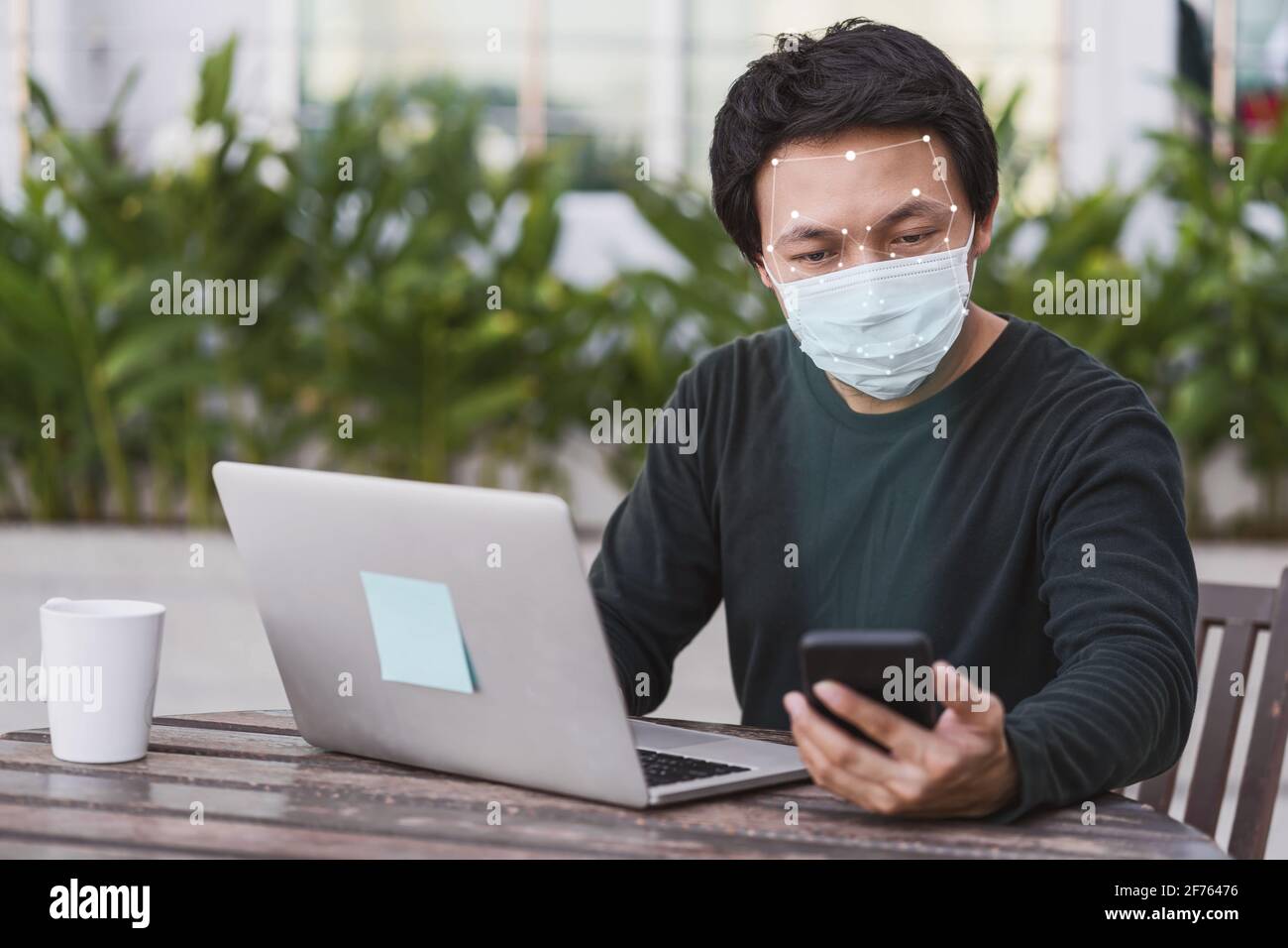 Asiatischer Geschäftsmann in legerer Kleidung mit Mobiltelefon für Biometrische Scans und Gesichtserkennung bei der Arbeit zu Hause, Technologie und Neuer normaler Covid-19 Stockfoto