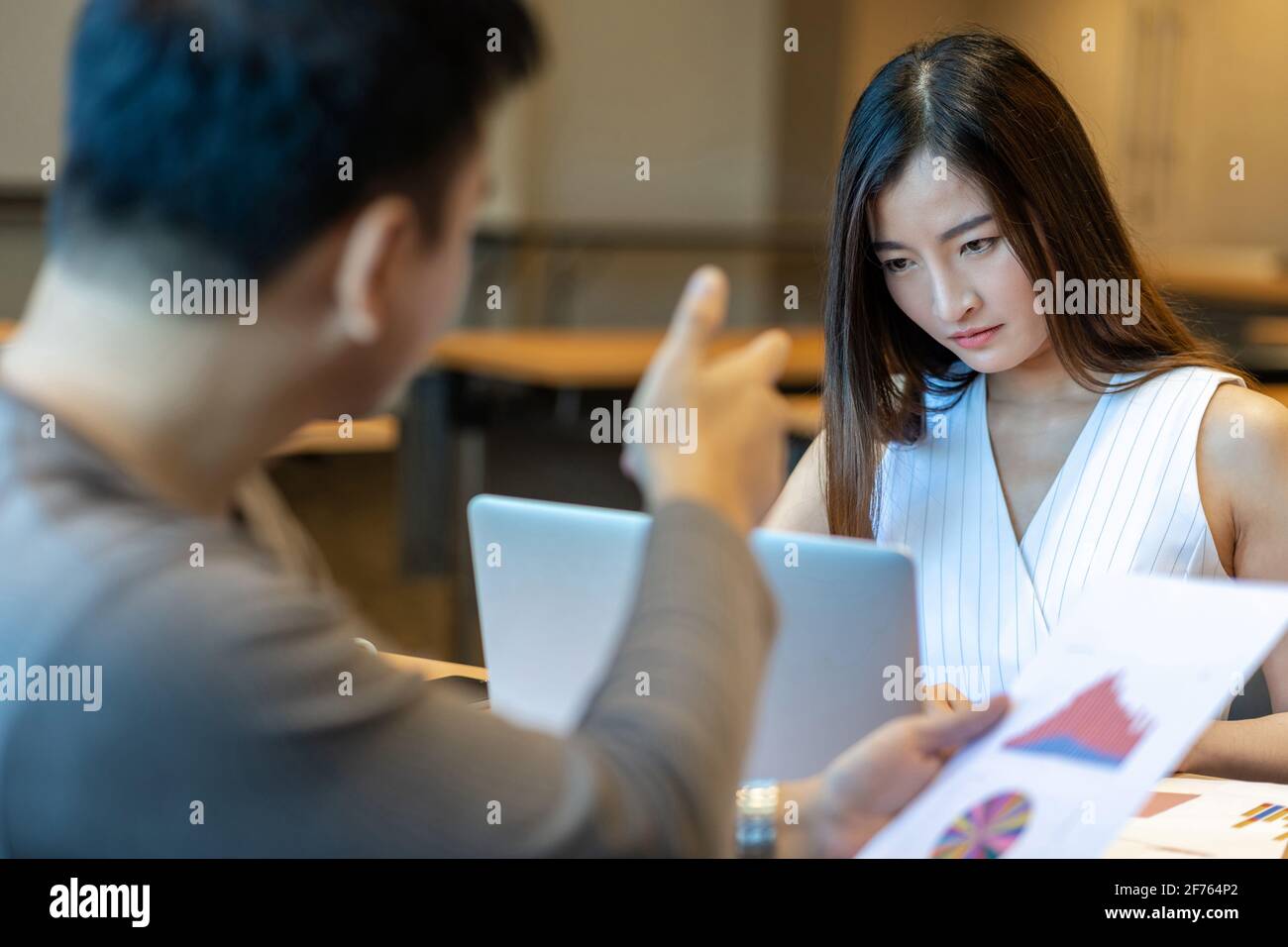 Rückansicht der Furious Chef schimpfen asiatische junge Geschäftsfrau in Casual Anzug von Punkt zu ihrem Gesicht über Leistung und KPI im modernen Büro, Business Stockfoto