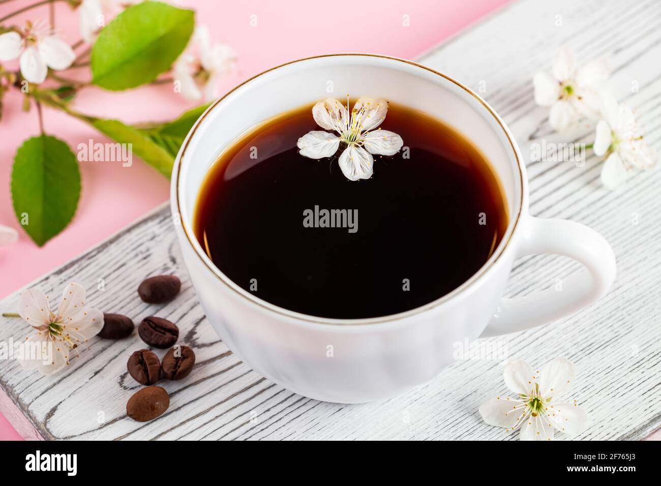 Starker Espresso-Kaffee auf weißem Holztablett. Frühlingsblumen eines Apfelbaums auf einem rosa Hintergrund. Guten Morgen und Frühling Konzept. Stockfoto