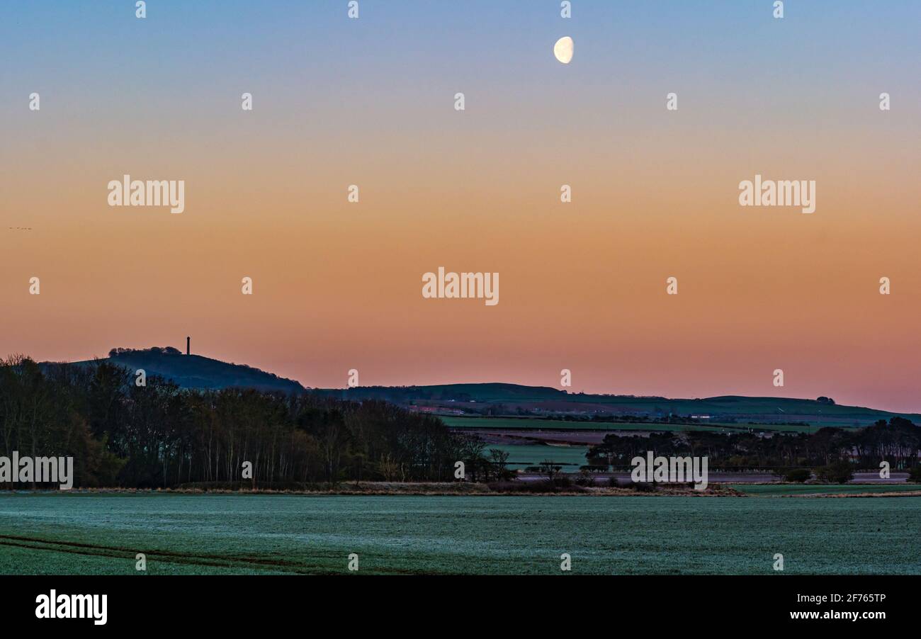 Vor Sonnenaufgang geht der Mond in frostiger Morgendämmerung über dem Byres Hill unter mit Blick auf das viktorianische Denkmal auf dem Hügel, East Lothian, Schottland, Großbritannien Stockfoto