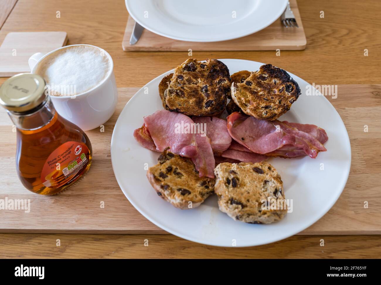 Frühstück oder Brunch mit heißen Brötchen mit Speck und Ahornsirup auf einem weißen Teller und Kaffee-Latte Stockfoto