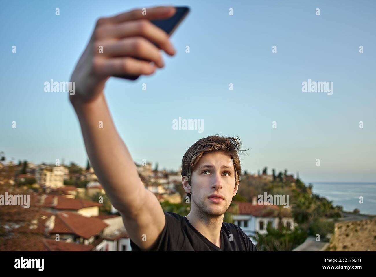 Der junge weiße Mann fotografiert sich mit dem Smartphone vor der Kulisse einer Altstadt von Antalya. Stockfoto