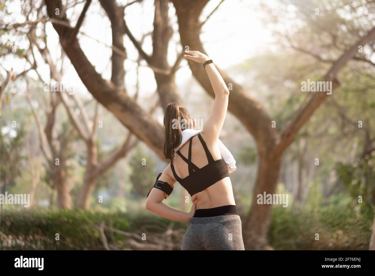 Eine athletische Frau, die sich vor einem Training aufwärmt, steht mit Blick auf den Am frühen Morgen aufgehende Sonne im Park Stockfoto