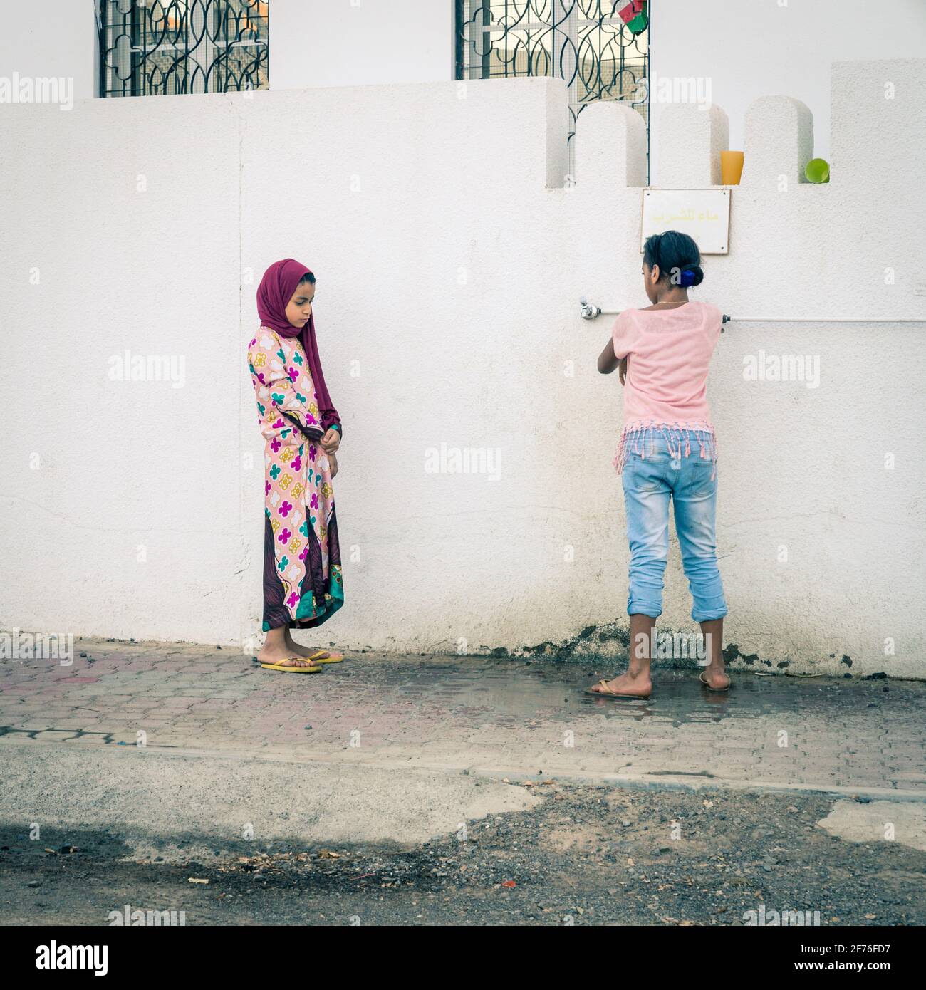 Maskat, Oman, 3. Dezember 2016: Zwei Mädchen an einem Wasserzapfen vor einer Moschee in der Altstadt von Maskat, Oman Stockfoto