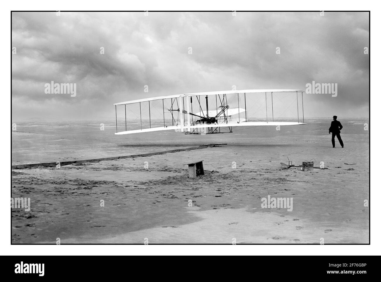 WRIGHT BROTHERS ERSTER MOTORBETRIEBENER FLUG ARCHIV 1900 Wright Brothers machen ersten motorisierten Flug 1903 Kitty Hawk, North Carolina, USA das Amerika-Foto zeigt den ersten motorisierten, kontrollierten, nachhaltigen Flug. Orville Wright an den Bedienelementen der Maschine, gestreckt auf dem unteren Flügel mit Hüften in der Wiege liegend, die den Wing-Warping-Mechanismus betätigte. Wilbur Wright läuft mit, um die Maschine zu balancieren, hat gerade seinen Halt an der nach vorne aufrechten Seite des rechten Flügels freigegeben. Hinter der Maschine sind die Startschiene, die Flügelstütze, eine Spulenbox und andere Elemente, die für die Flugvorbereitung benötigt werden, sichtbar. Stockfoto