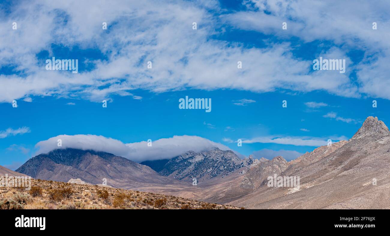 Brauner karger Berg trifft auf blauen Berg, der in Wolken unter einem blauen Himmel gehüllt ist. Stockfoto