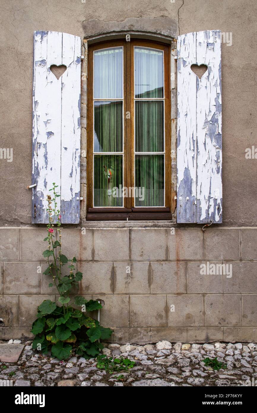 Ein Fenster und hölzerne Fensterläden mit abblätternder Farbe auf einem Haus in Charroux, Allier, Frankreich Stockfoto