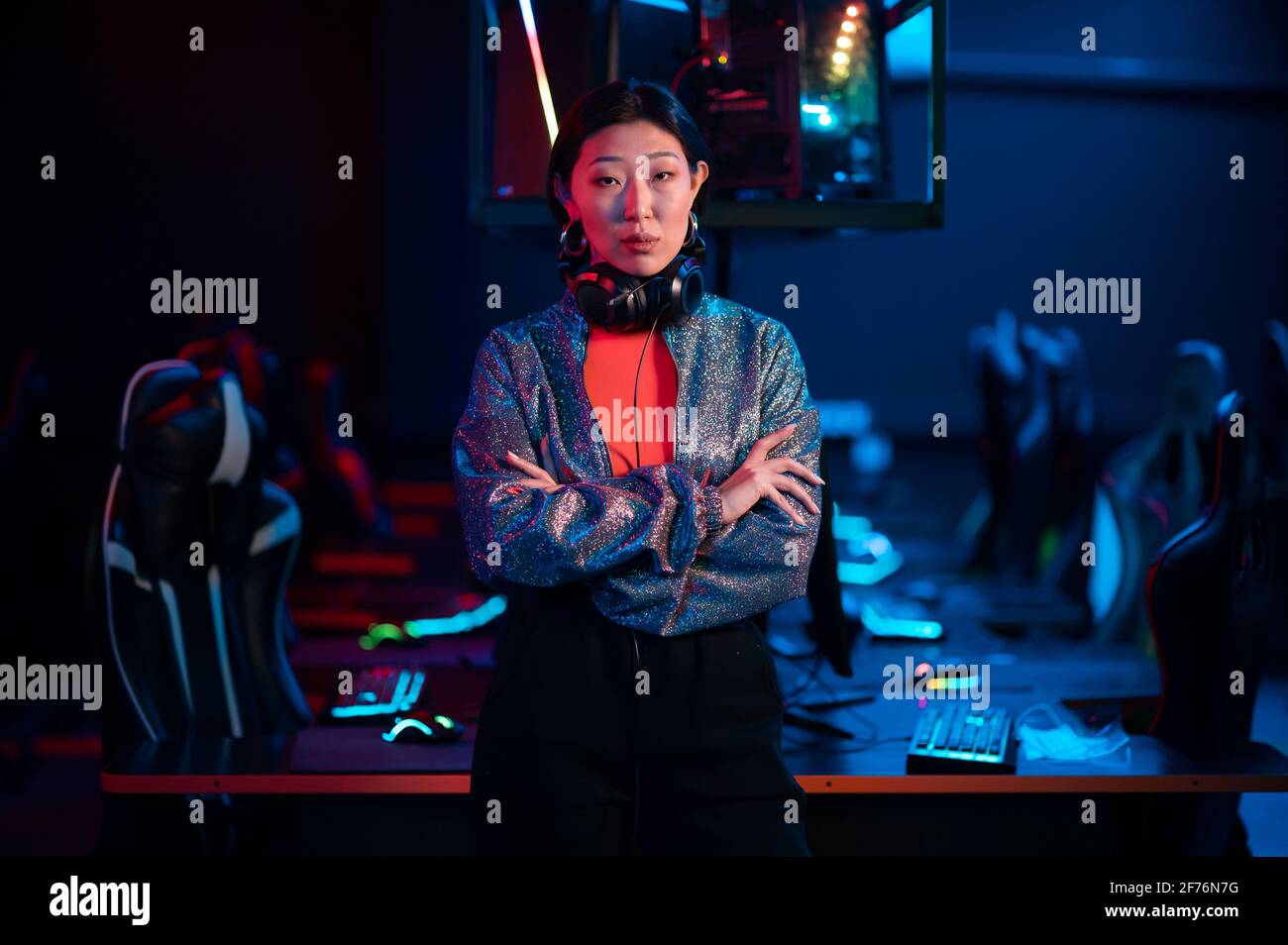 Die junge asiatische Gamerin im Headset posiert mit gefalteten Armen für die Kamera. Stockfoto