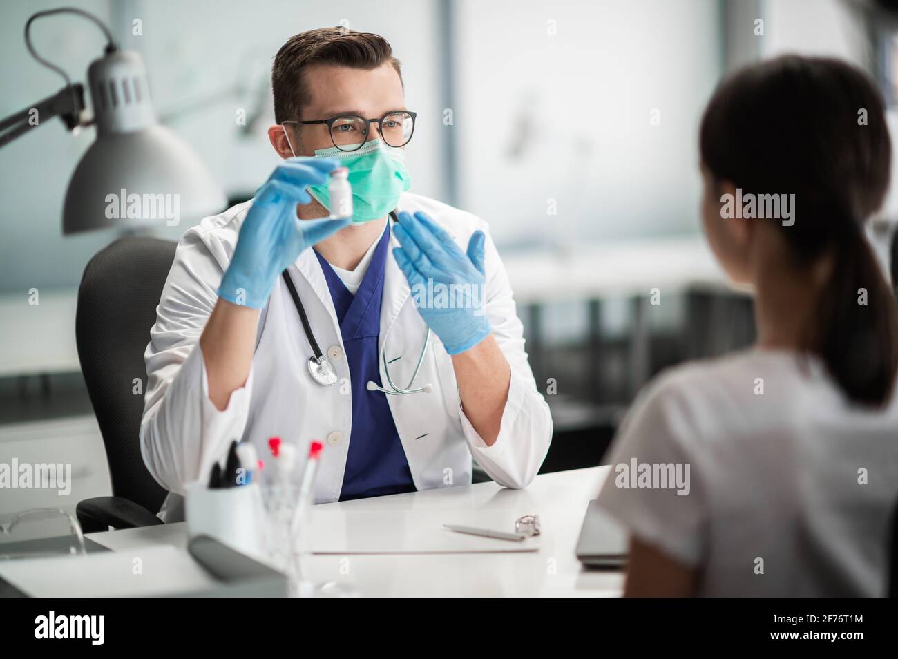 Zur Vorbeugung von Covid-19 bietet ein junger Arzt einer Frau einen Impfstoff in einer Flasche mit nachgewiesener Wirksamkeit an. Stockfoto