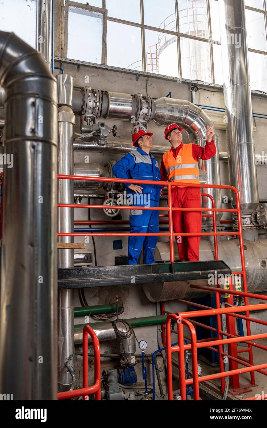 Wartungstechniker, der neben dem Ölarbeiter in der Ölraffinerie mit großen Rohrleitungen steht. Stockfoto