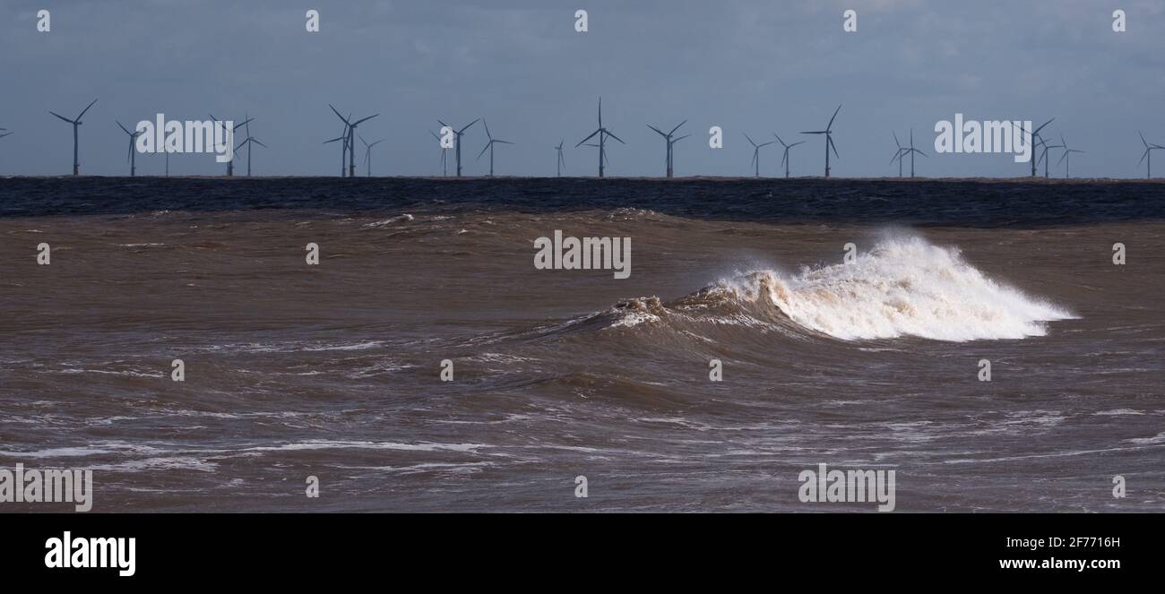 Die Wellenmacht der Nordsee auf der Lincolnshire Küste mit Windturbinen in der Ferne, die die Bereitstellung ermöglichen Erneuerbare und nachhaltige Energie Stockfoto