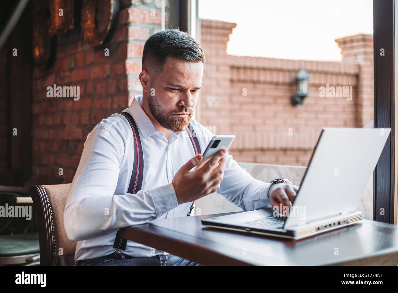 Junger Geschäftsmann, der auf sein Telefon schaut. Laptop auf dem Tisch vor ihm Stockfoto