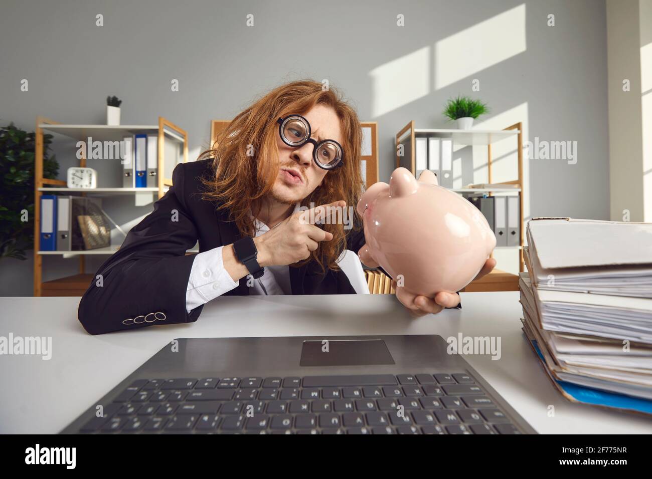 Lustige junge seltsame Mann Buchhalter zeigt auf Sparschwein mit Finger Stockfoto