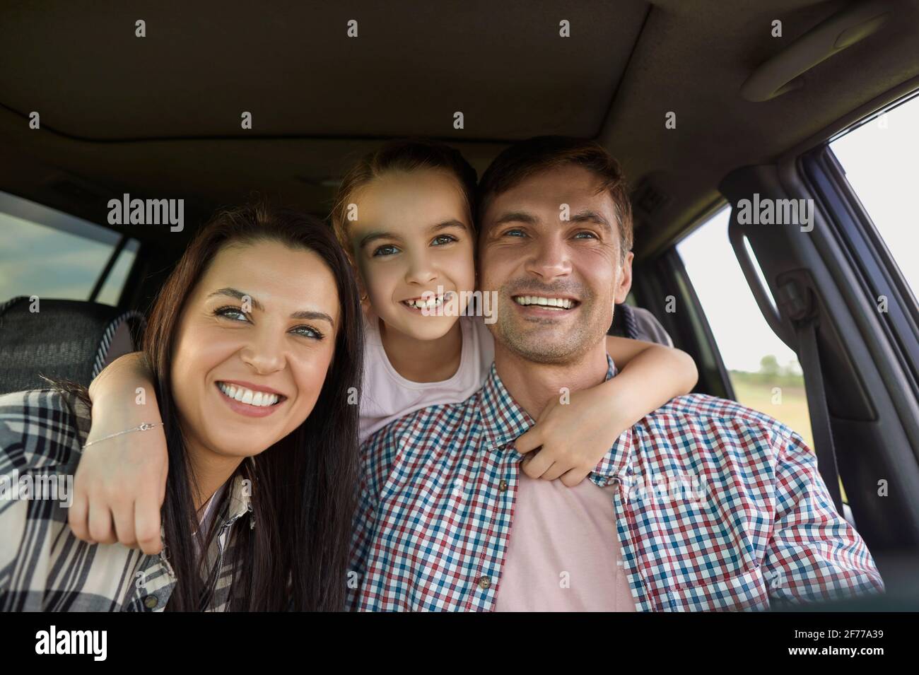 Porträt einer fröhlichen Familie mit Kind auf dem Autoreise. Mädchen umarmt ihre jungen Eltern in der Auto während der Sommerferien Stockfoto